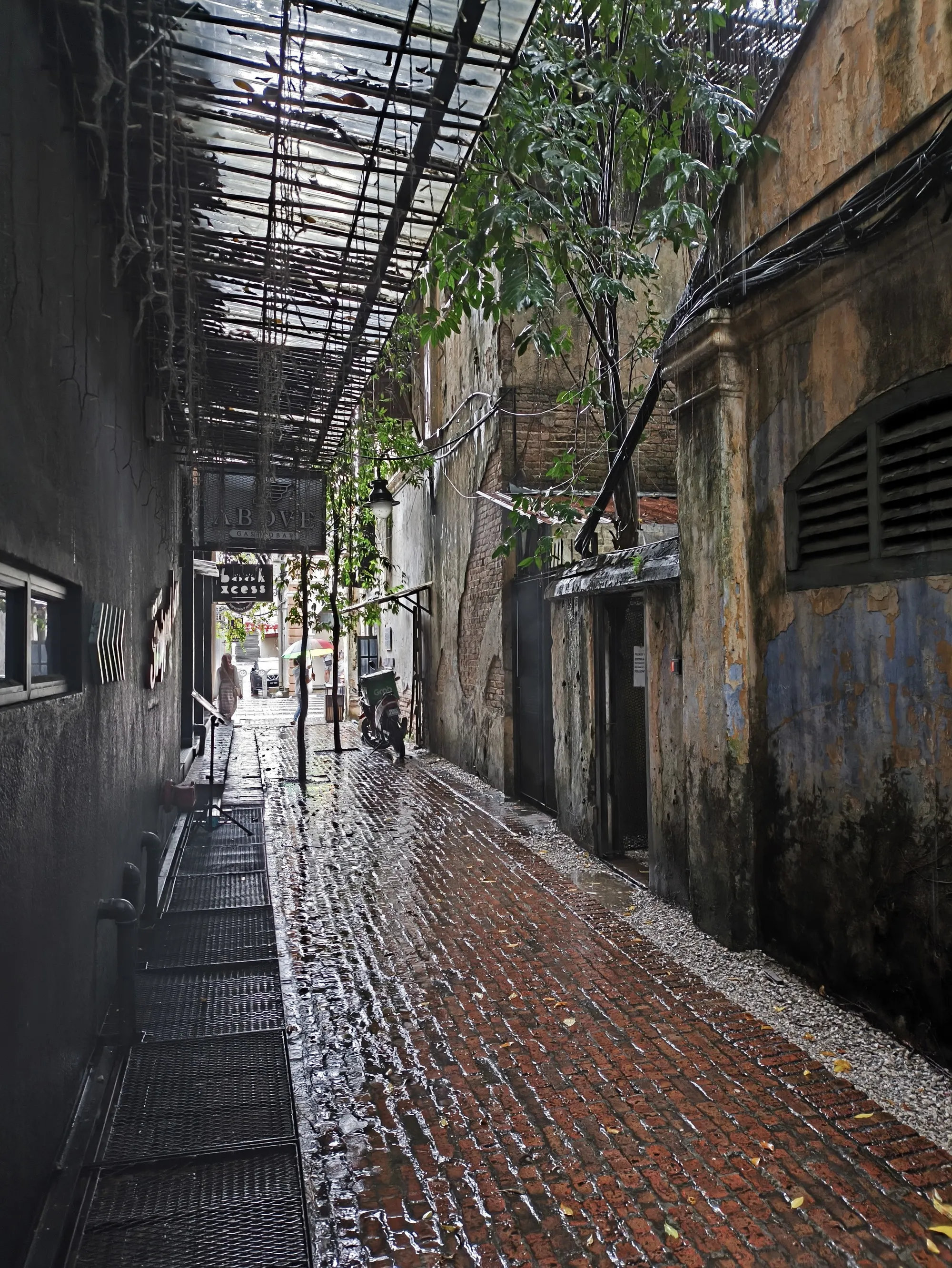 Rain-wet brick paving between weathered shophouse walls under a covered walkway in Concubine Lane