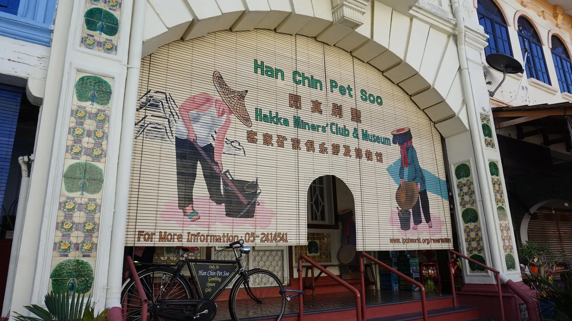 Arched shophouse facade with bamboo blinds painted with miners, signed Han Chin Pet Soo Hakka Miners' Club and Museum