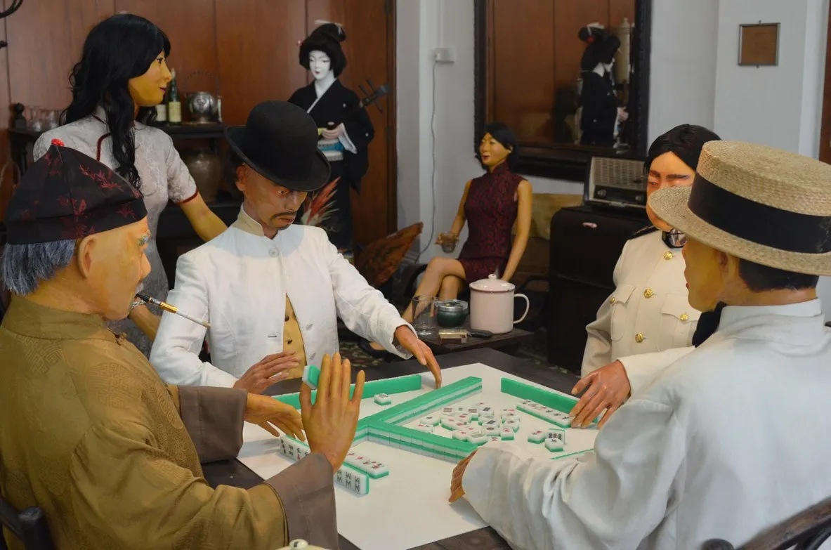 Museum diorama of men in period dress playing mahjong at a table, with women standing behind them