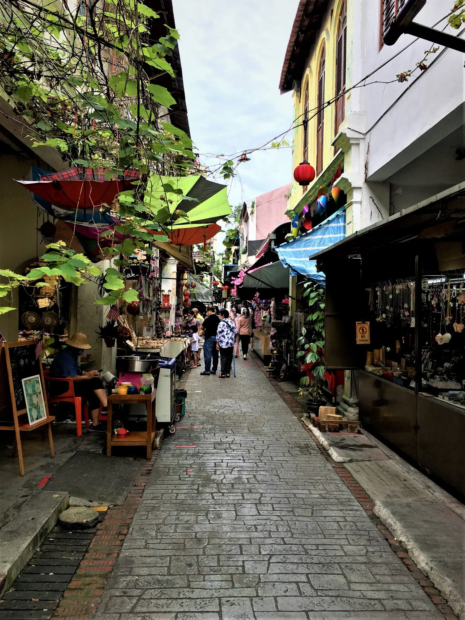 Narrow stone-paved heritage lane in Ipoh Old Town between shophouses, with hanging umbrellas and small stalls