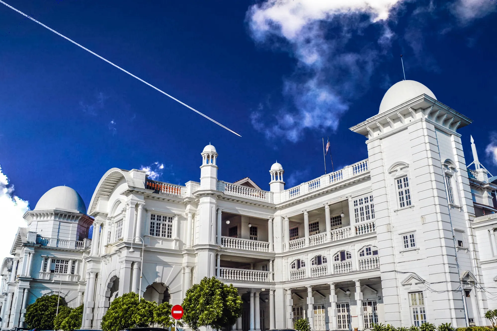 Low-angle view of the white domes and arched verandas of Ipoh Railway Station under a deep blue sky