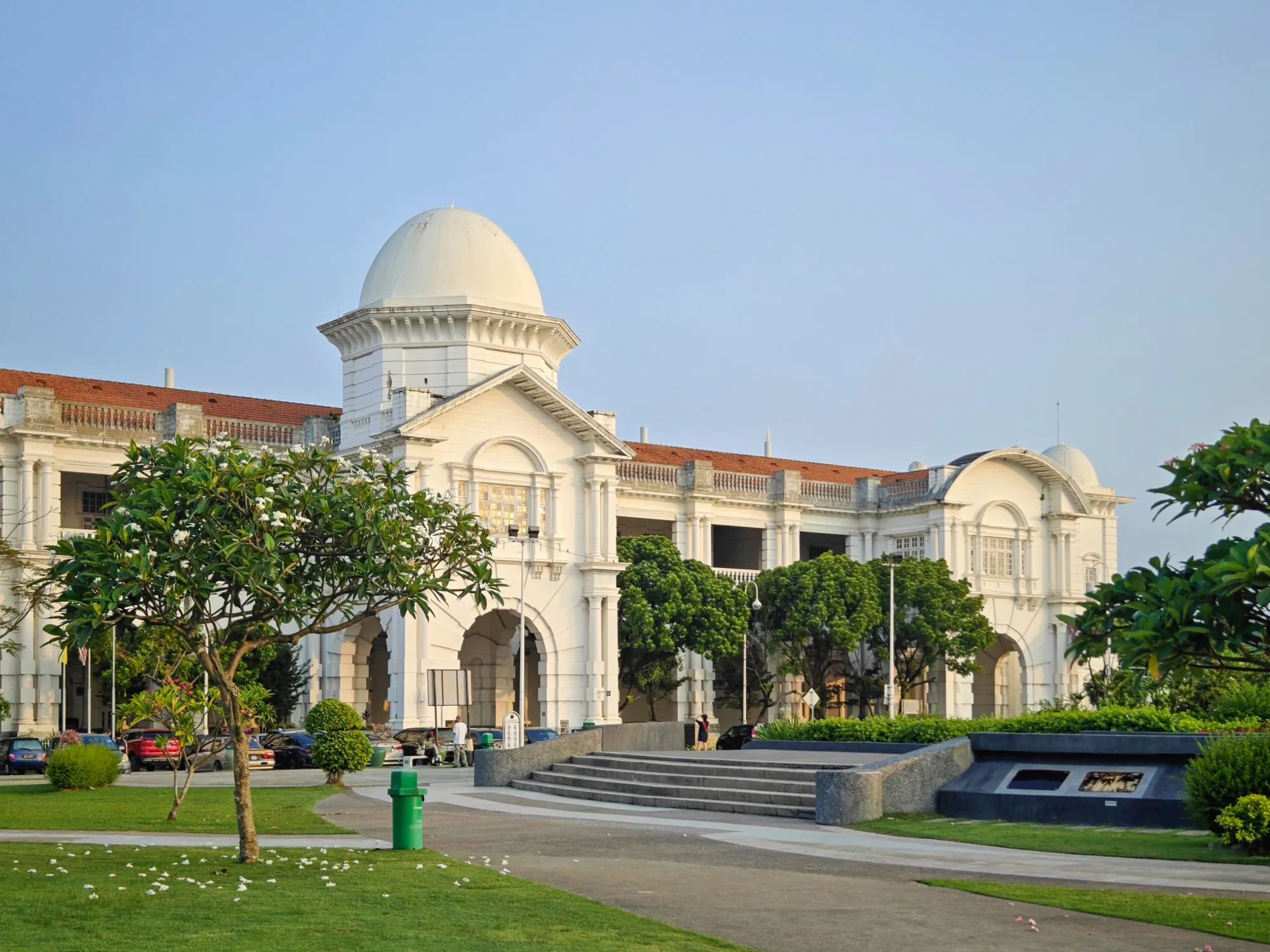 White colonial-era Ipoh Railway Station with domes and arches behind a lawn and palms