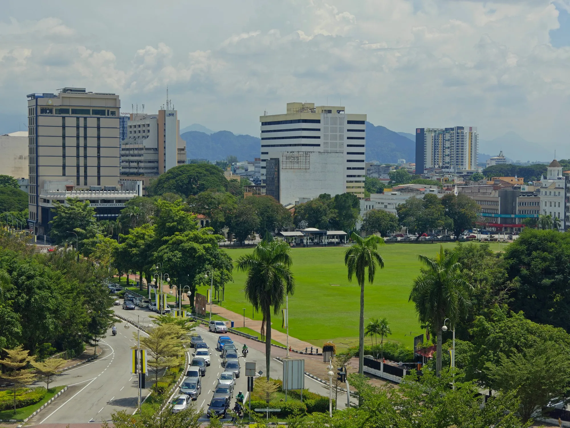 Downtown Ipoh skyline with a green padang, palm trees and forested hills in the background