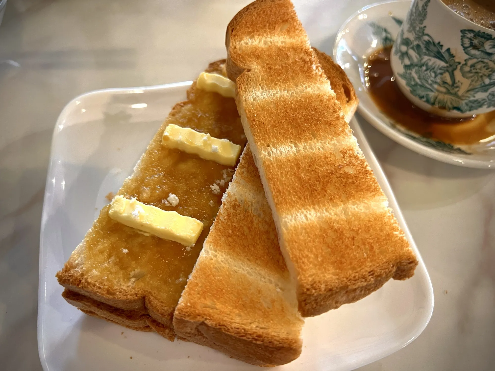Plate of toasted bread slices filled with kaya and butter on a marble-pattern table