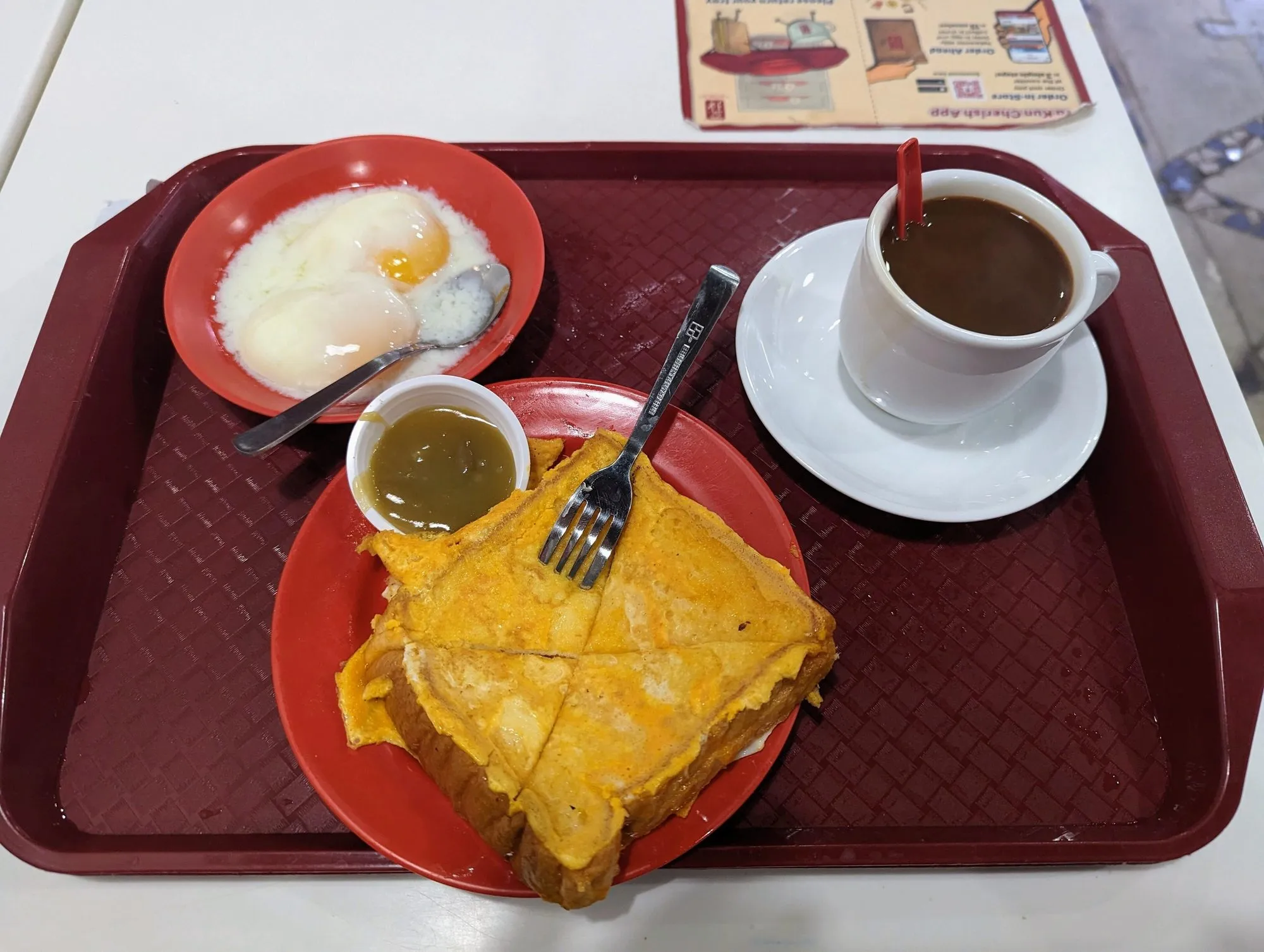 Breakfast tray with two soft-boiled eggs, a cup of coffee and toast with a small cup of kaya