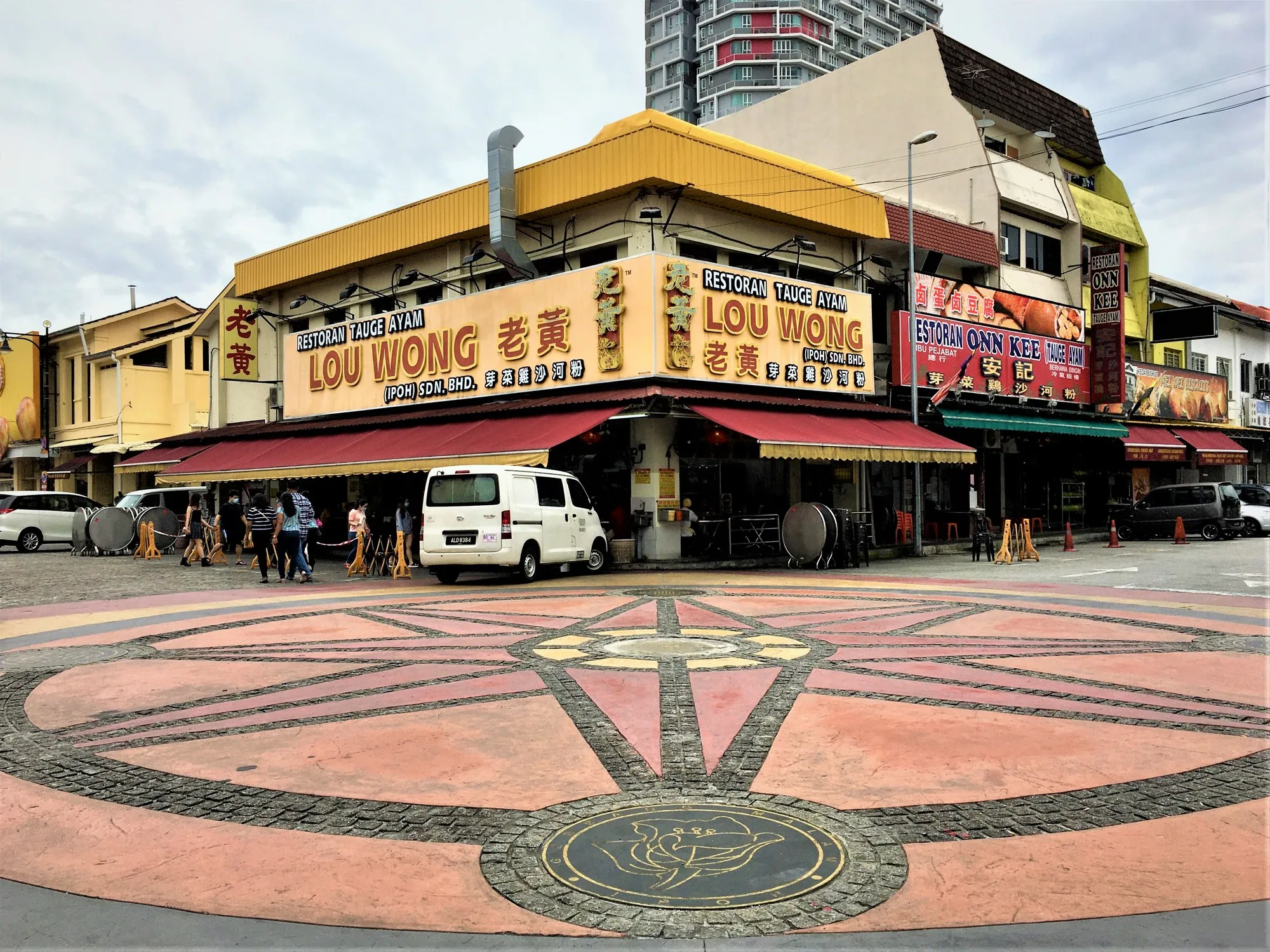 Corner shophouse restaurant with yellow signage and a patterned paved square on Jalan Yau Tet Shin, Ipoh