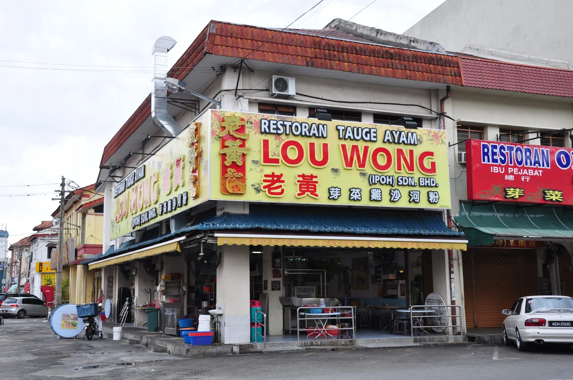 Corner shophouse restaurant in Ipoh Old Town with a yellow Lou Wong sign and open-front tables under a blue awning
