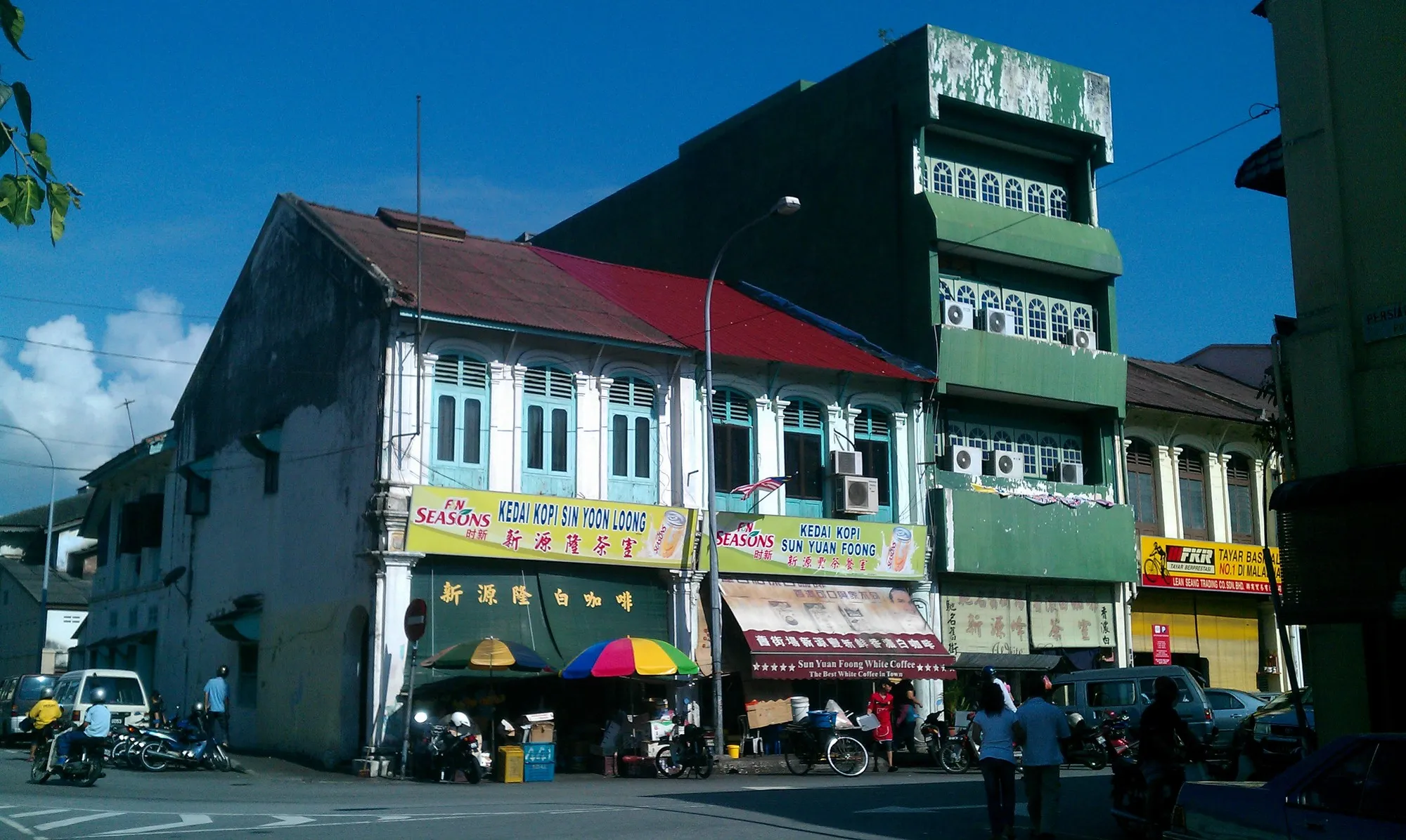 Row of old shophouses with coffee shop awnings on Jalan Bandar Timah in Ipoh Old Town under a blue sky