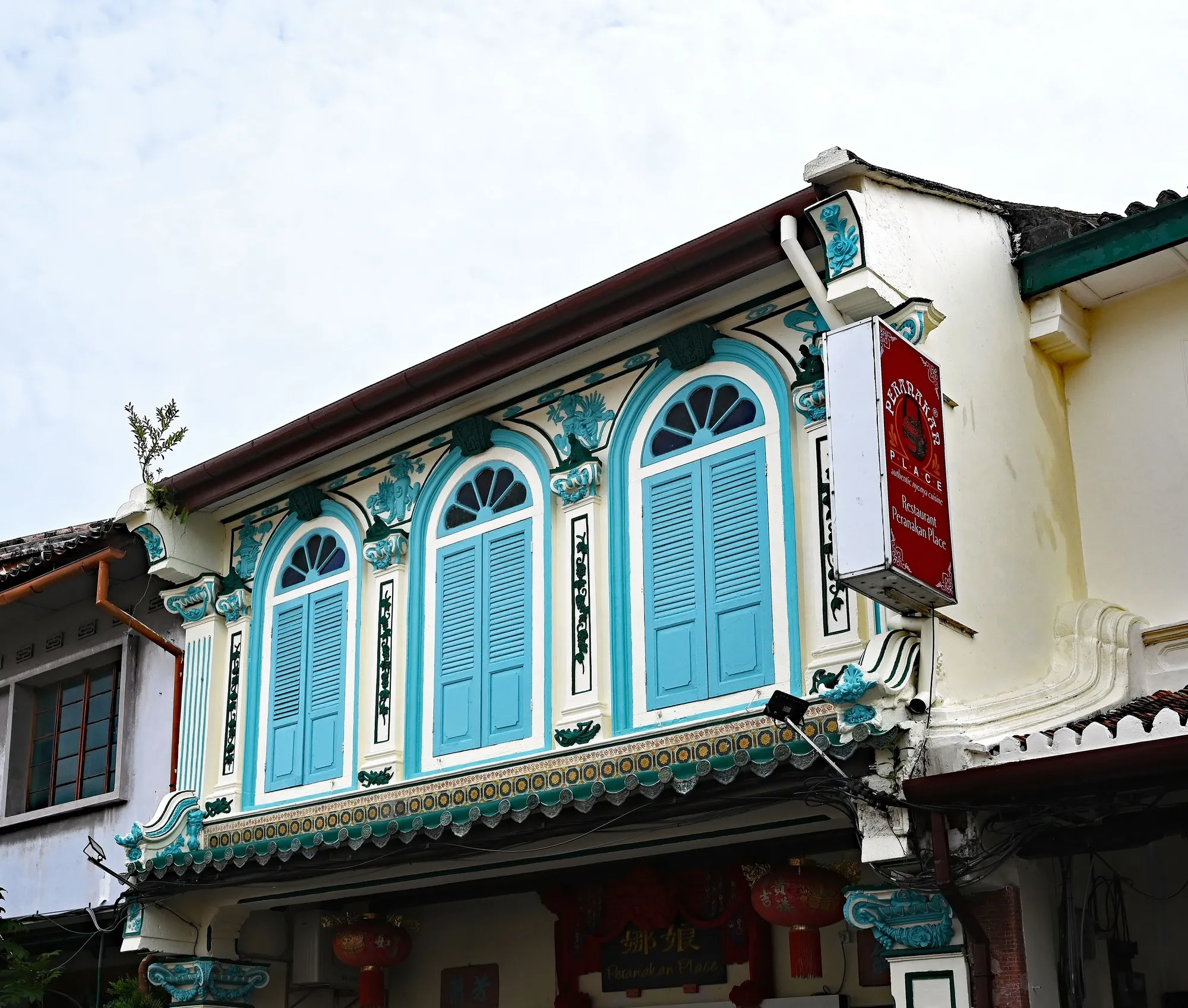 Ornate Peranakan-style shophouse in Melaka with blue-shuttered arched windows, green tiles and plaster mouldings