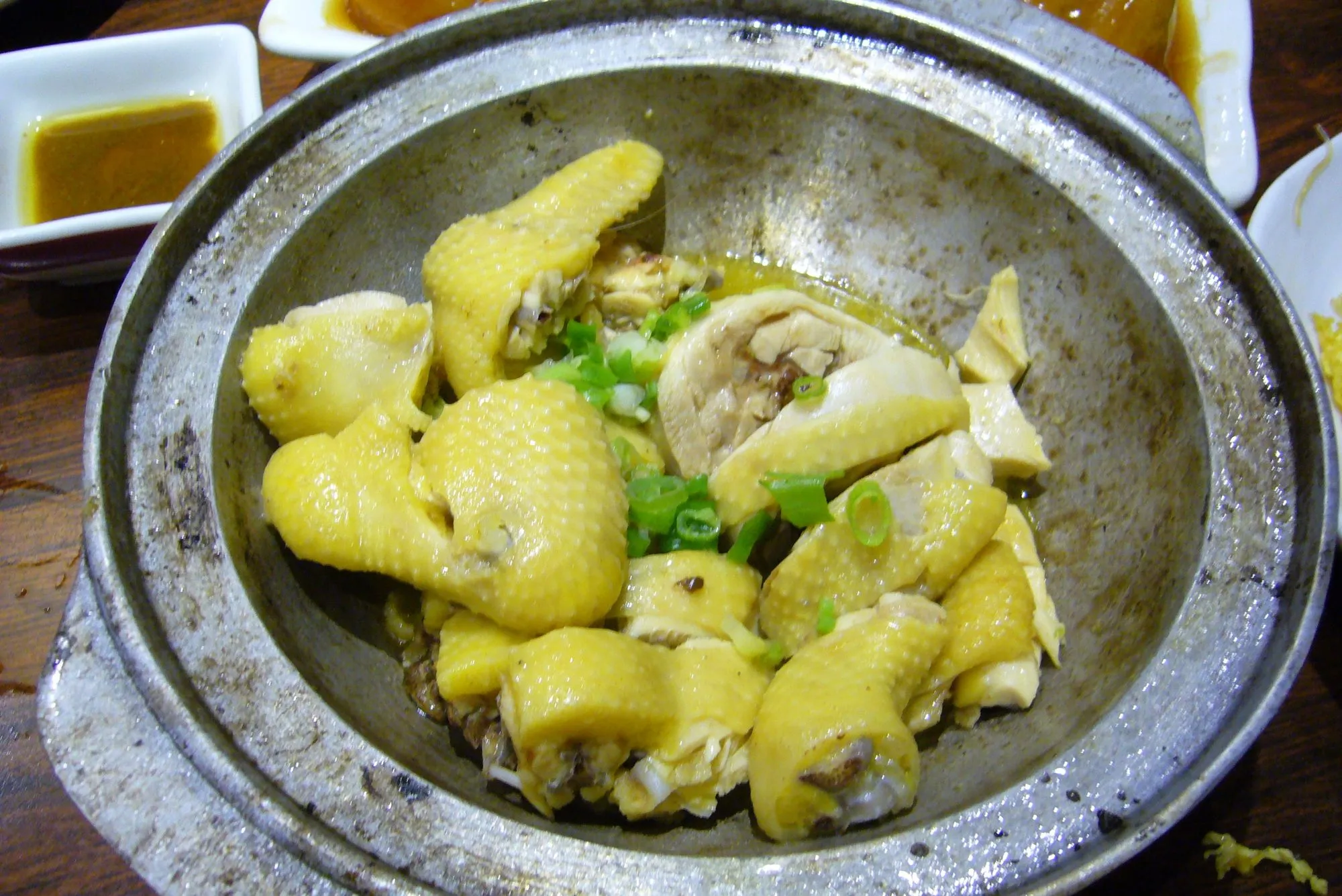 Chopped yellow-skinned salt-baked chicken in a metal pot with spring onion